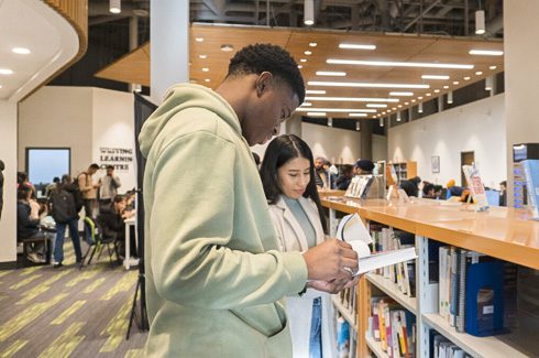 Two students looking at books in the library